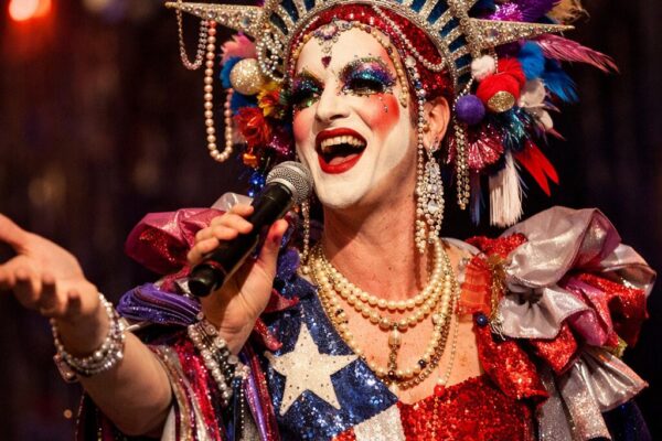 Drag performer in sparkling red, white, and blue costume with jeweled crown and microphone